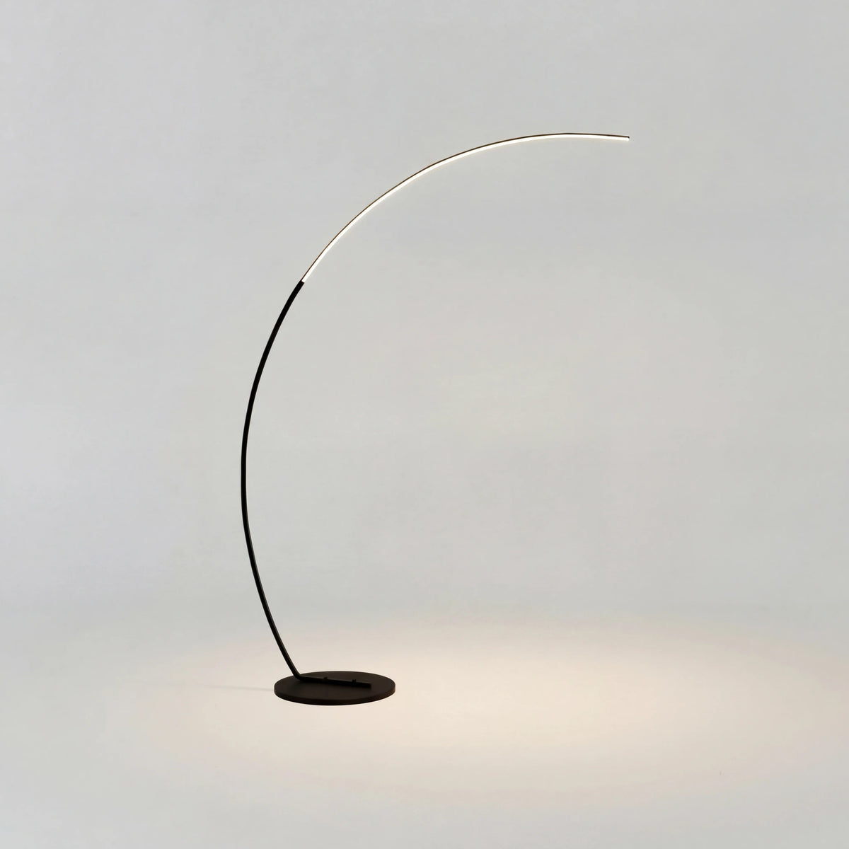 Bågformad golvlampa i pulverlackerad aluminium som böjer sig över en soffa